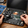 Technician performing professional laptop maintenance by cleaning internal components, fans, and RAM modules using precision tools and isopropyl alcohol.