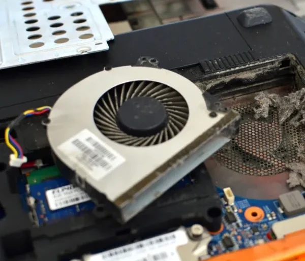 Dusty laptop cooling fan removed for cleaning to solve overheating and airflow problems during laptop repair service.