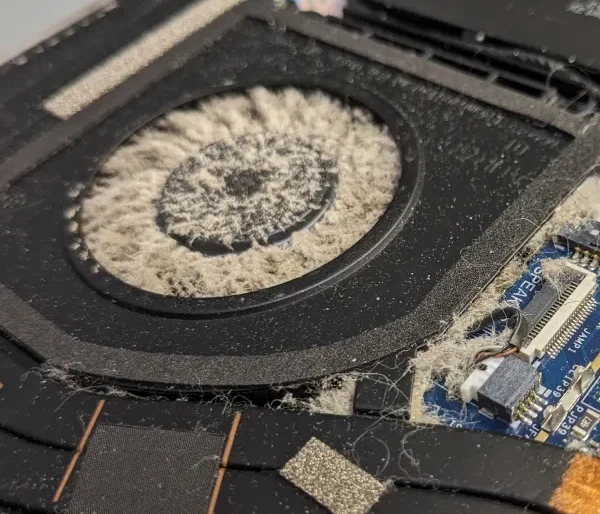 Technician carefully brushing dust off electronic circuits on a laptop motherboard to prevent overheating and improve performance.